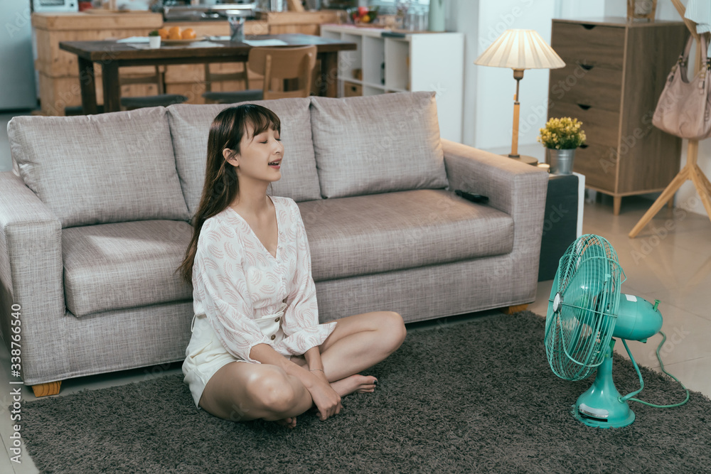 hot summer day taiwanese woman sitting on living room carpet with appliance to chill. asian young la