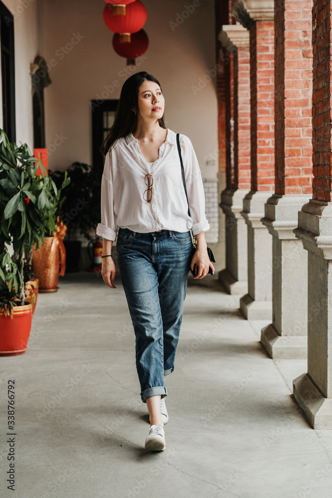 full length of asian woman in casual wear walking in corridor walkway and looking aside in tradition