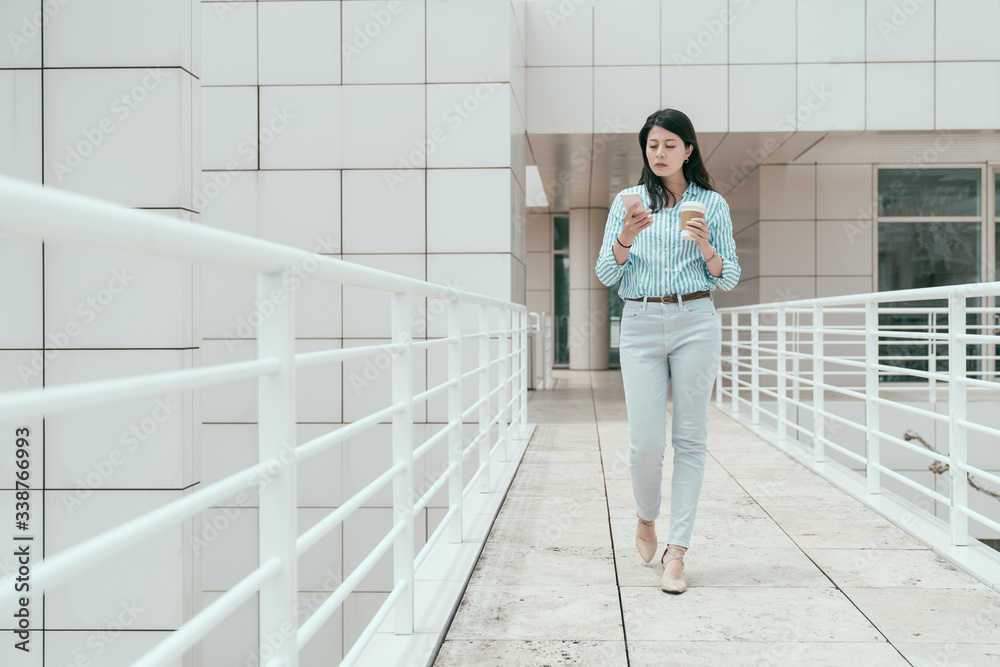 full length of elegant young office lady walking in sky corridor outdoor in skyscraper. confident fe