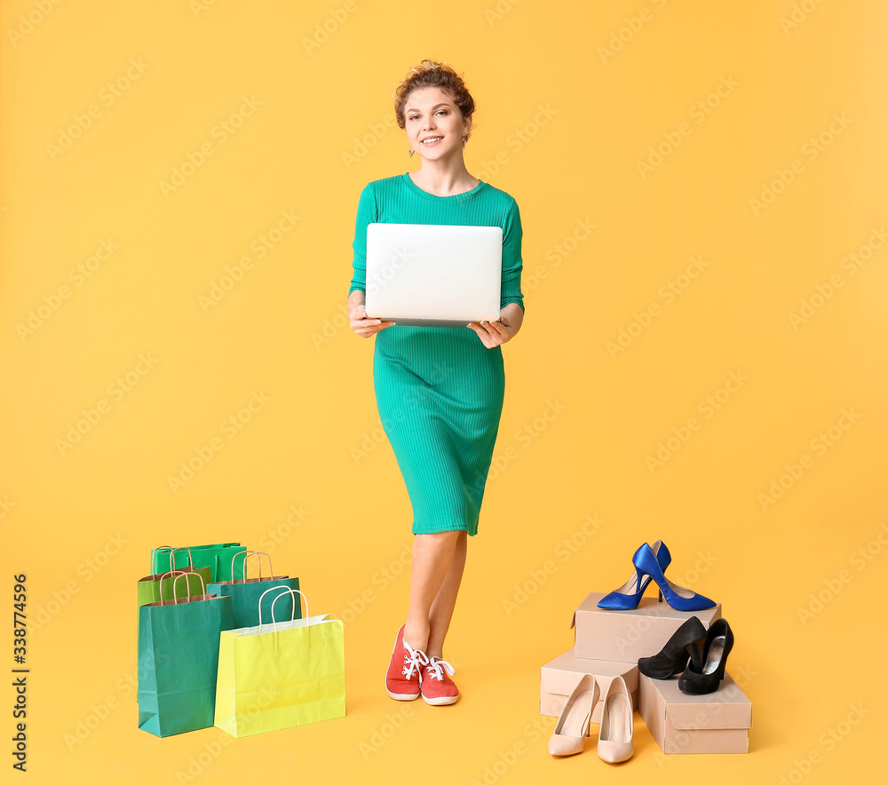 Young woman with laptop and shopping bags on color background