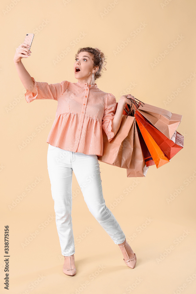 Surprised young woman with mobile phone and shopping bags on color background