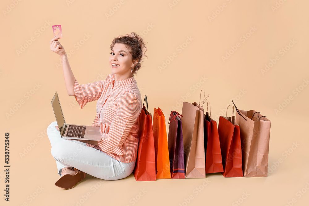 Beautiful young woman with laptop, credit card and shopping bags on color background