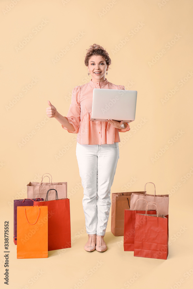 Beautiful young woman with laptop and shopping bags on color background