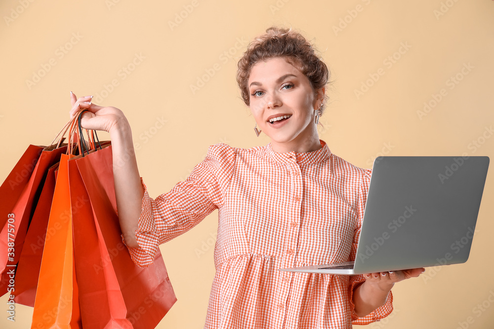 Beautiful young woman with laptop and shopping bags on color background