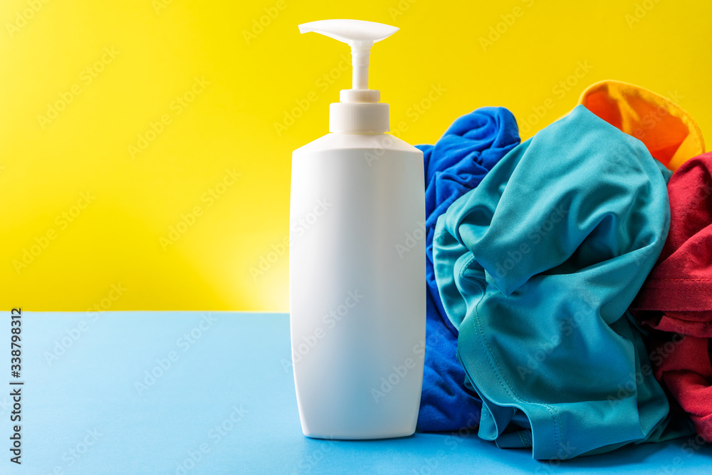 Plastic bottles of cleaning products set with pile clothes on blue table Yellow background.