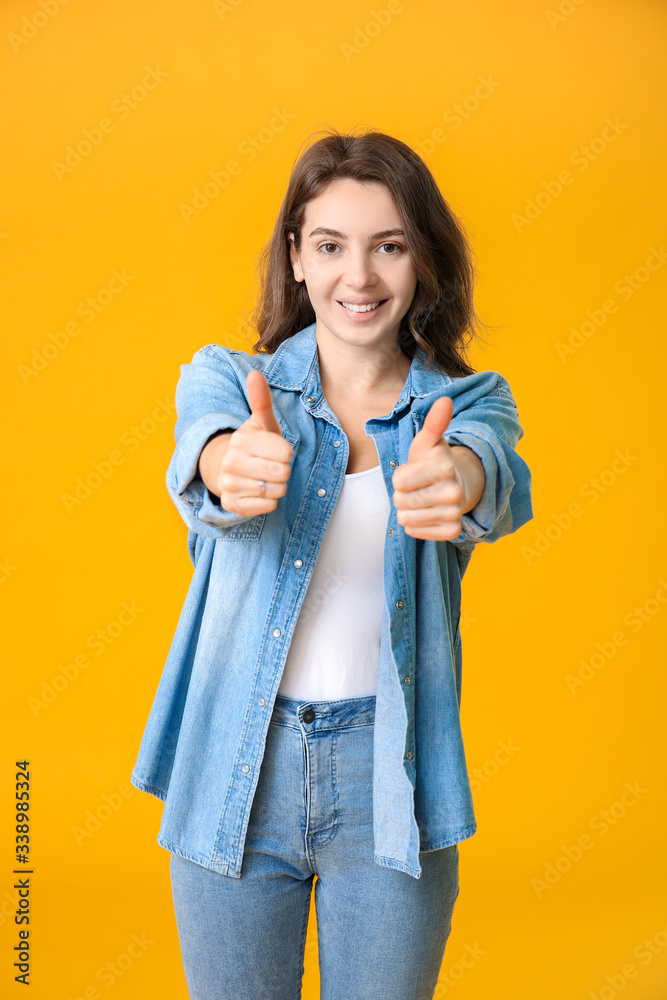 Beautiful young girl showing thumb-up on color background