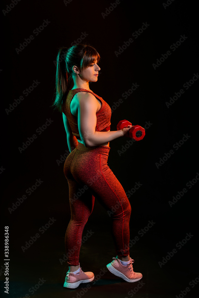 Sporty muscular woman with dumbbells on dark background