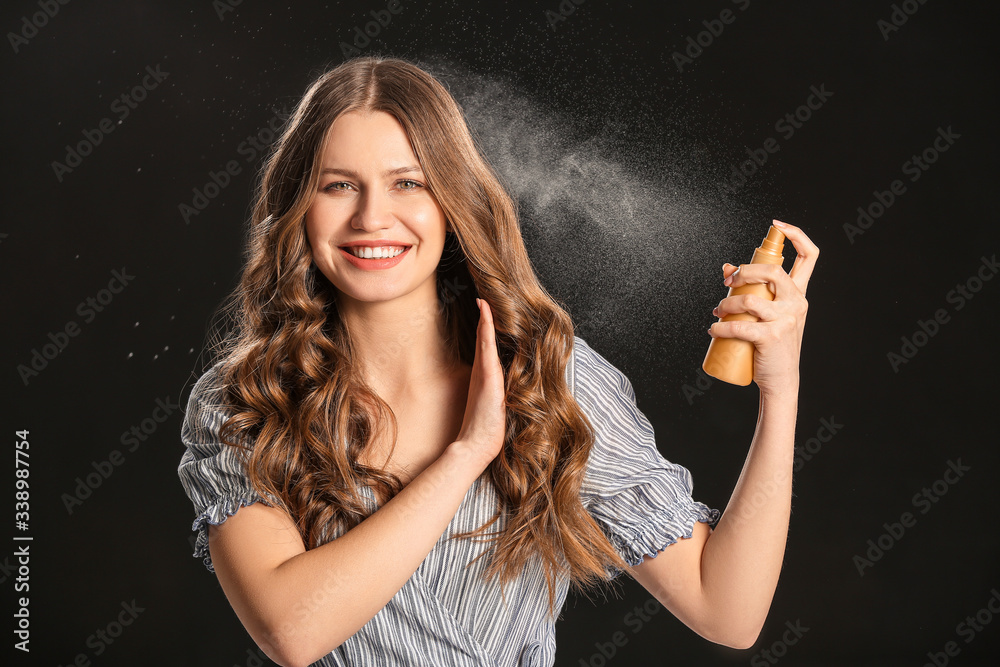 Beautiful young woman with hair spray on dark background