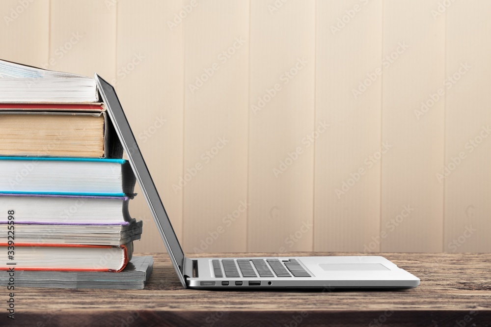 Stack of books with modern laptop on table