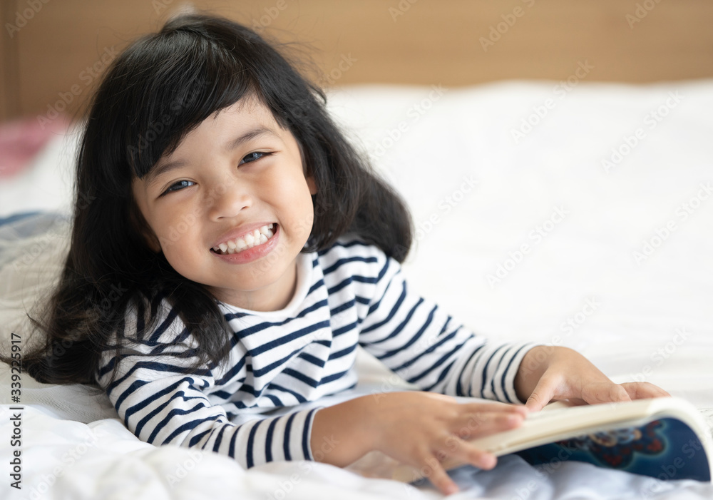 Little cute child girl lying on the bed and reading a book. education concept.