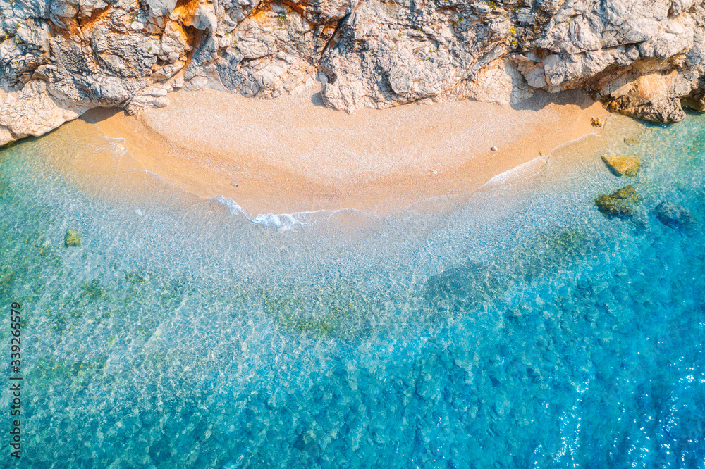 Aerial view of sandy beach with rocks and sea with transparent blue water at sunset. Coast of adriat