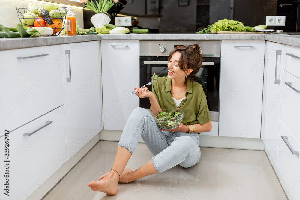 女人坐在家里的厨房地板上吃健康沙拉。素食、健康和