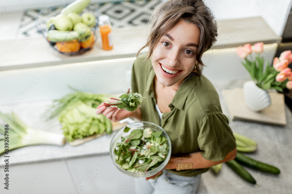 一位年轻开朗的女士站在厨房里吃沙拉，上面放着食材的肖像