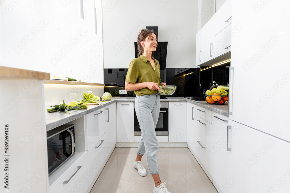 女人在家里的现代厨房里烹饪健康食品，室内视野开阔。女人是运动模糊的