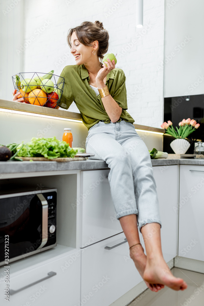 Full length portrait of a young and cheerful woman with healthy raw food on the kitchen at home. Veg