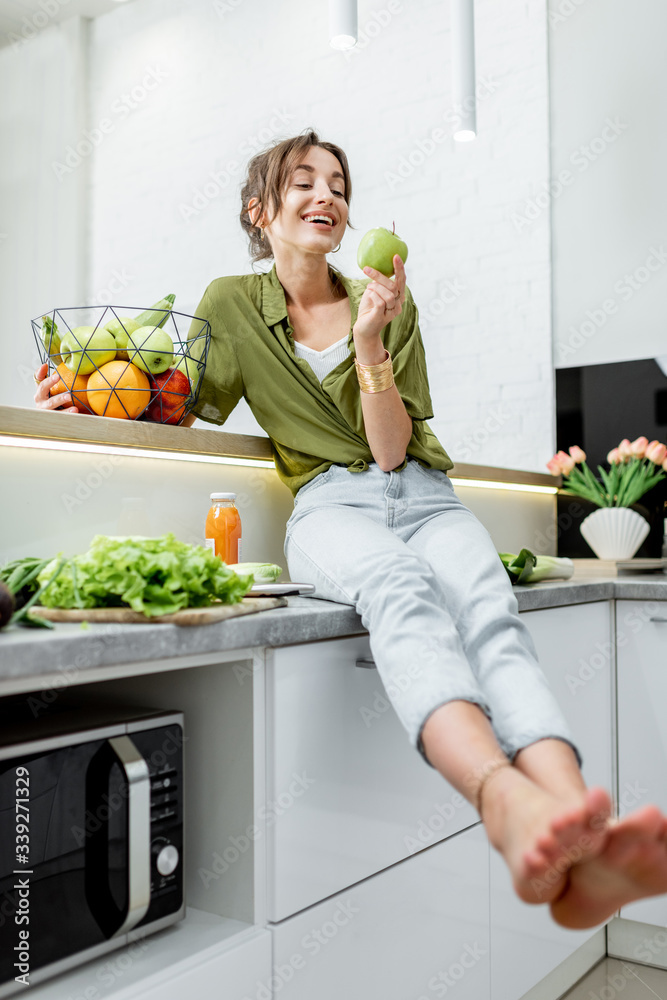 Full length portrait of a young and cheerful woman with healthy raw food on the kitchen at home. Veg