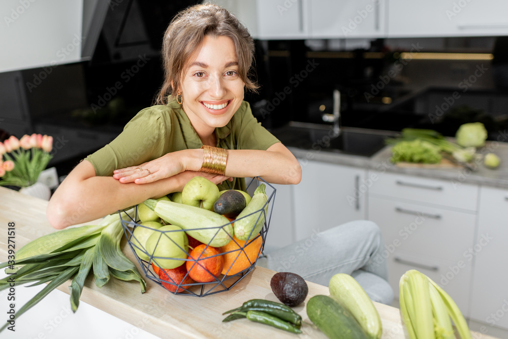 一个年轻快乐的女人的画像，家里的厨房里有健康的生食。素食主义，