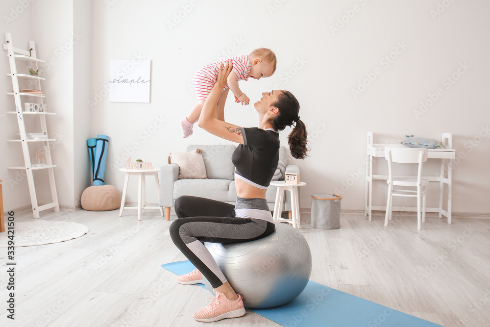 Young sporty mother and her baby doing exercises with fitball at home