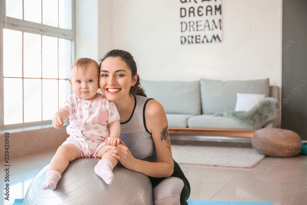 Young sporty mother and her baby doing exercises with fitball at home