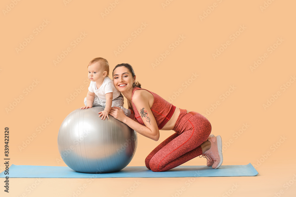 Young sporty mother and her baby doing exercises with fitball on color background