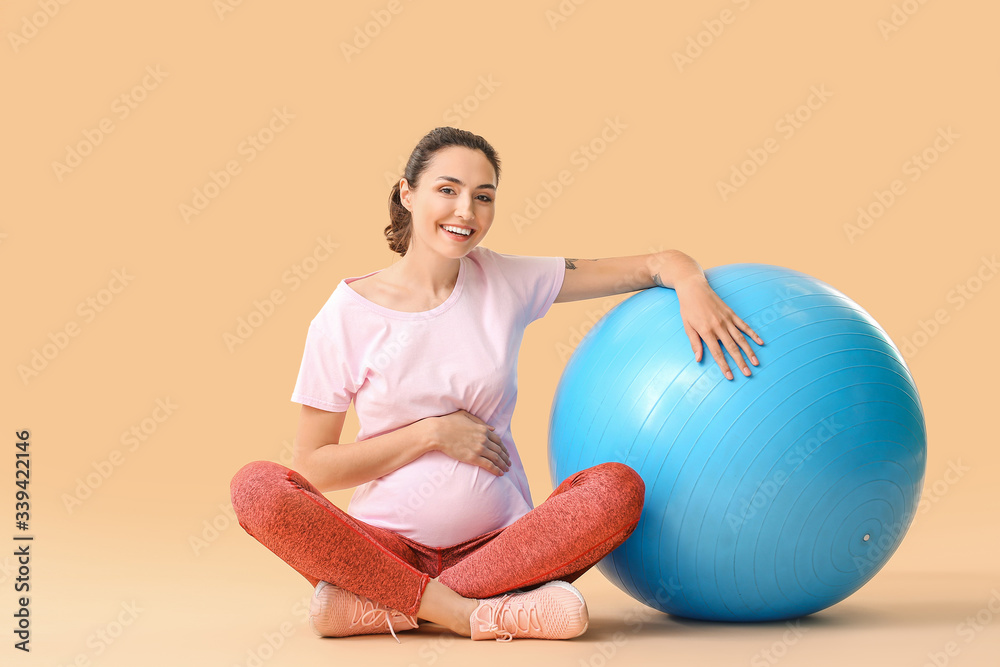 Young pregnant woman doing exercises with fitball on color background