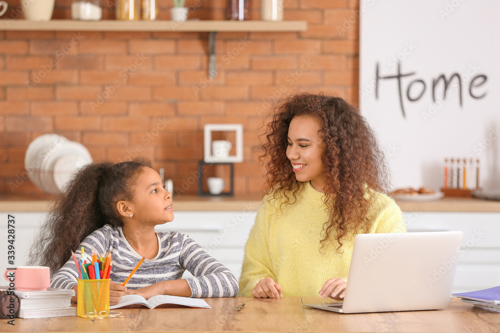 Little African-American girl with her mother doing homework in kitchen