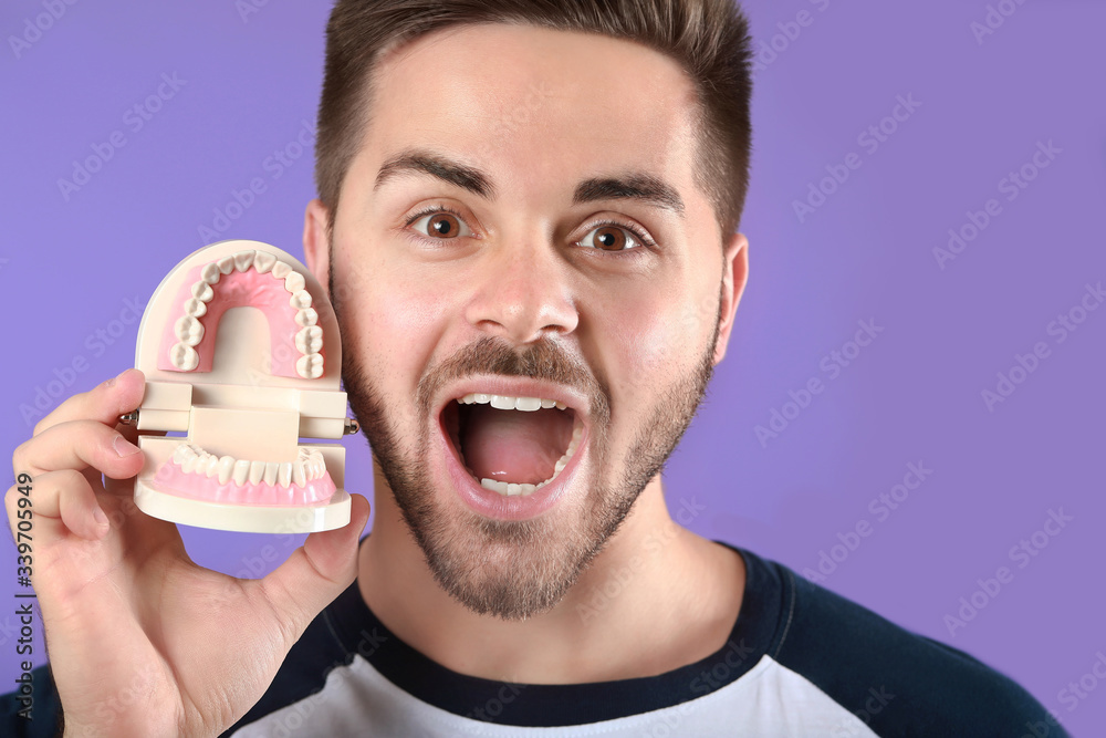 Happy young man with plastic jaw model on color background