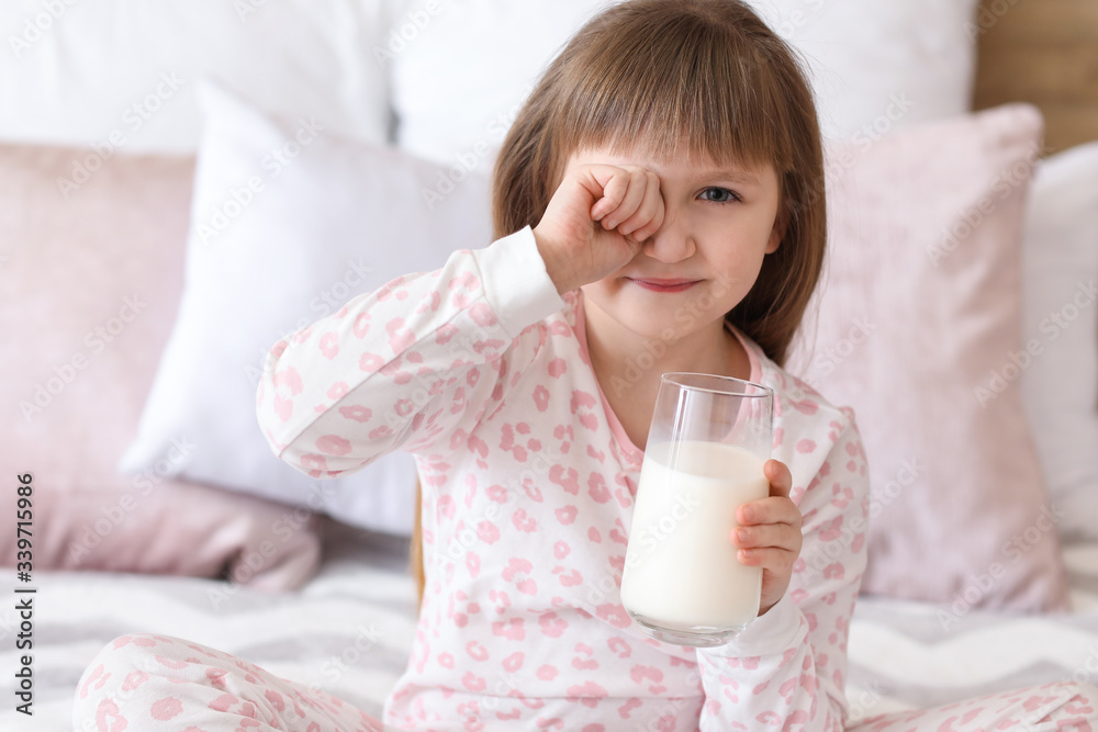 Sleepy little girl with glass of milk in bedroom