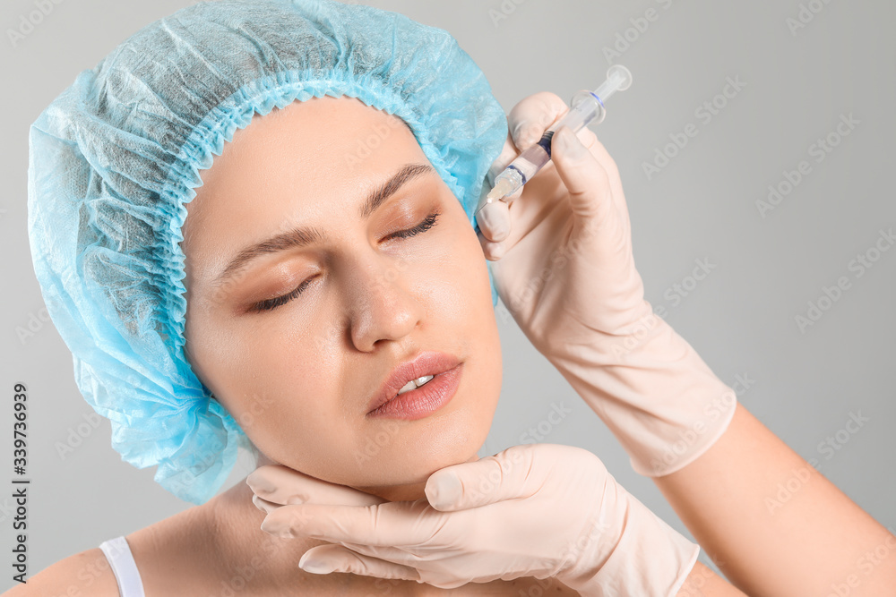 Young woman receiving filler injection on grey background