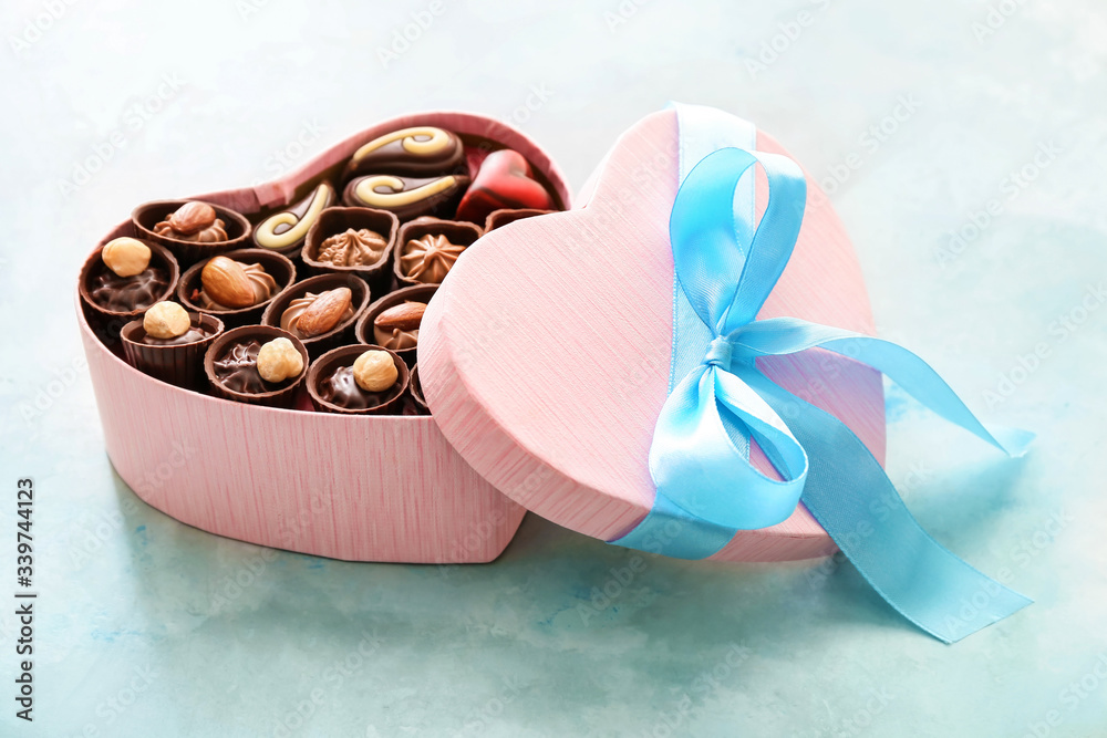 Heart-shaped box with delicious candies on color background