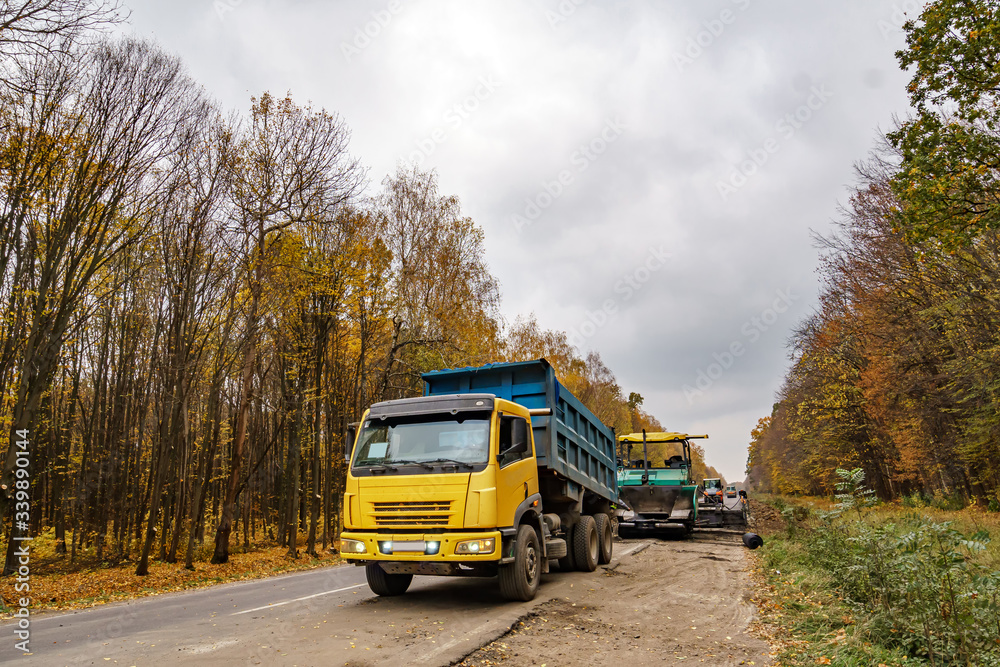 Road repair. Laying new asphalt. Heavy special machines. Truck in operation. Side view. Closeup.