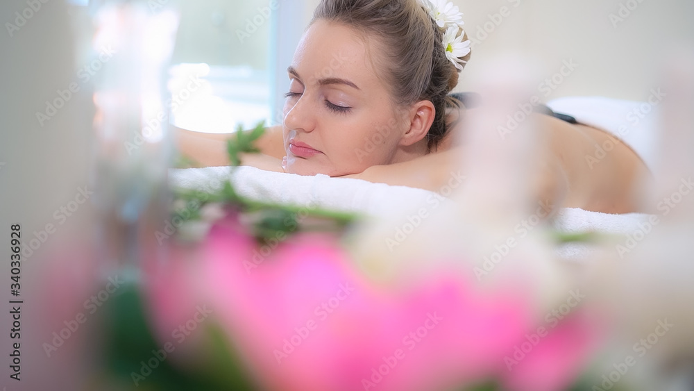 Woman getting hot stone massage treatment by professional beautician therapist in spa salon. Luxury 