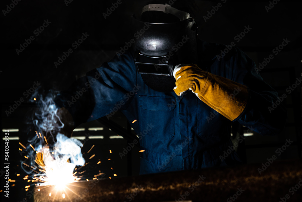 Metal welder working with arc welding machine to weld steel at factory while wearing safety equipmen