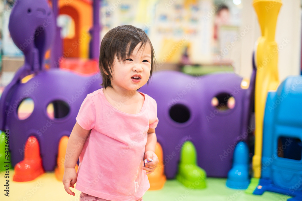 Little cute Asian toddler girl standing and looking somethings at playground. Kid enjoy exploring ne