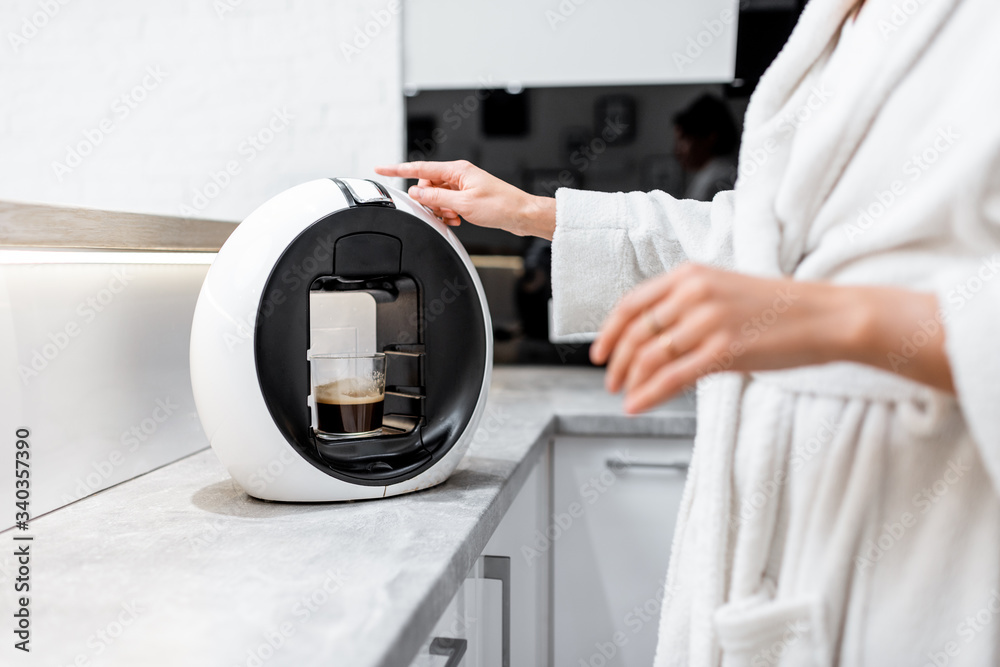 Young woman in bathrobe making coffee with a coffee machine on the kitchen at home, cropped view wit