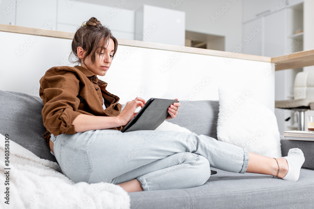 Young relaxed woman working or surfing the internet on a digital tablet while sitting on the couch a