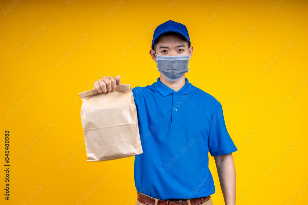 Young Asian handsome delivery man wearing mark holding a food paper bag on right hand over yellow is