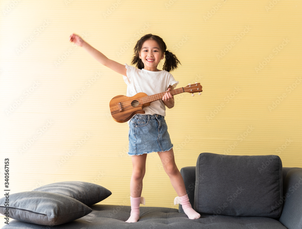 cute little girl playing ukulele on sofa with fun, inspiration for kids want to be musician star