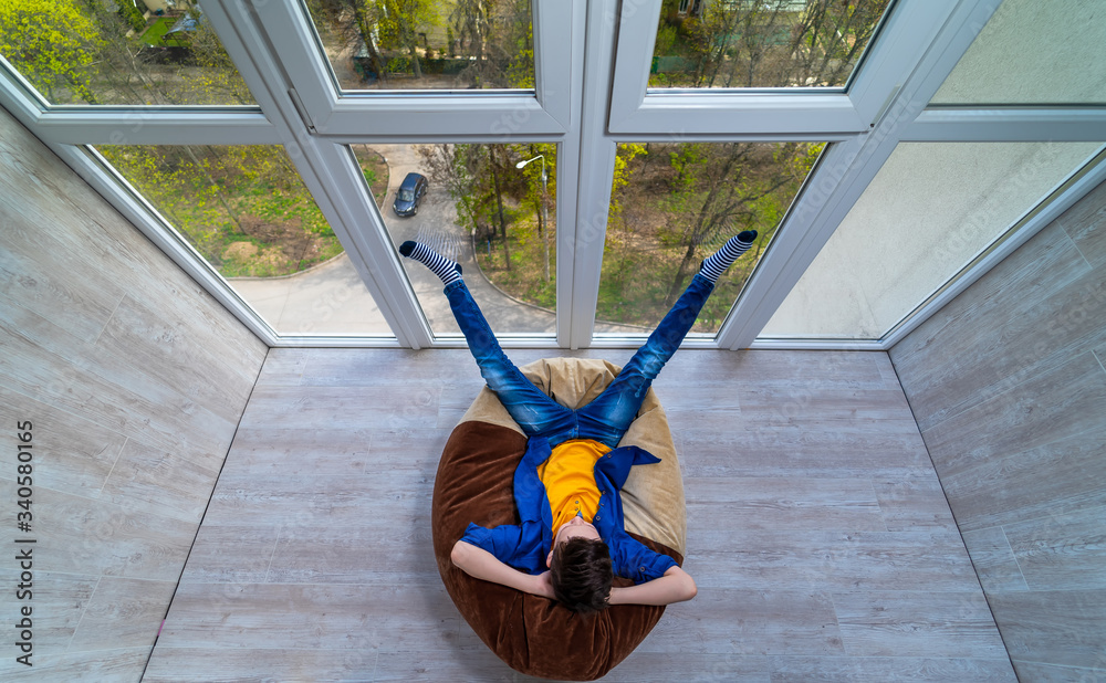 Little boy relaxing on a terrace. Teenage dreaming of summer vocation looking through the glass wall