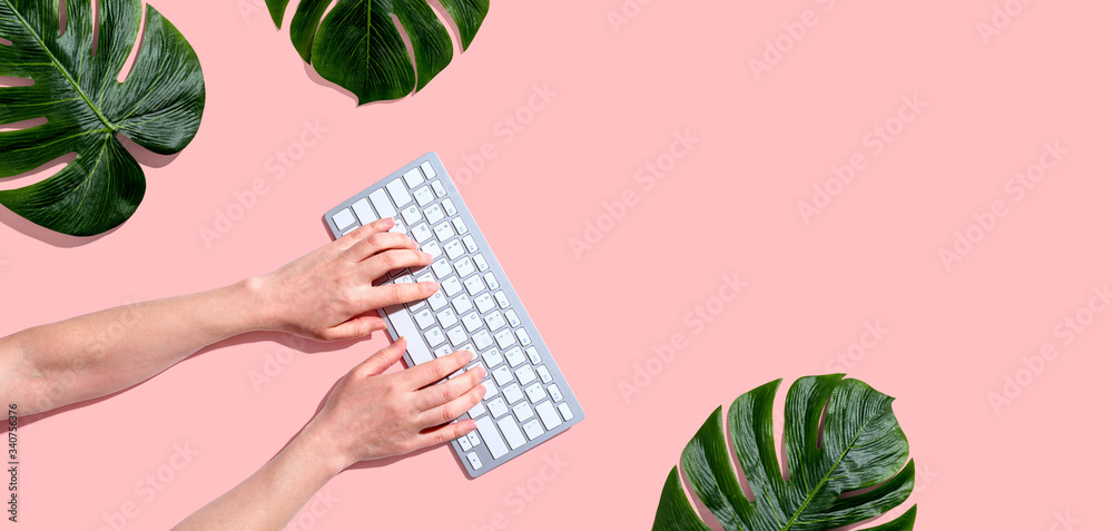 Person using a computer keyboard with tropical leaves from above