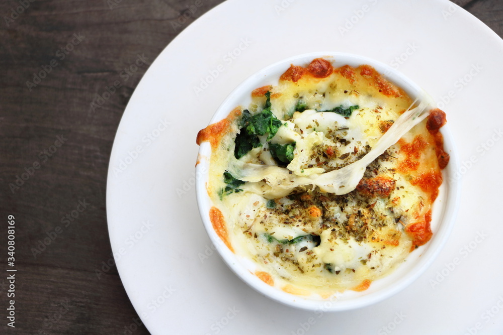 Top view of baked spinach with cheese in white bowl and white plate on wooden table, Flat lay style