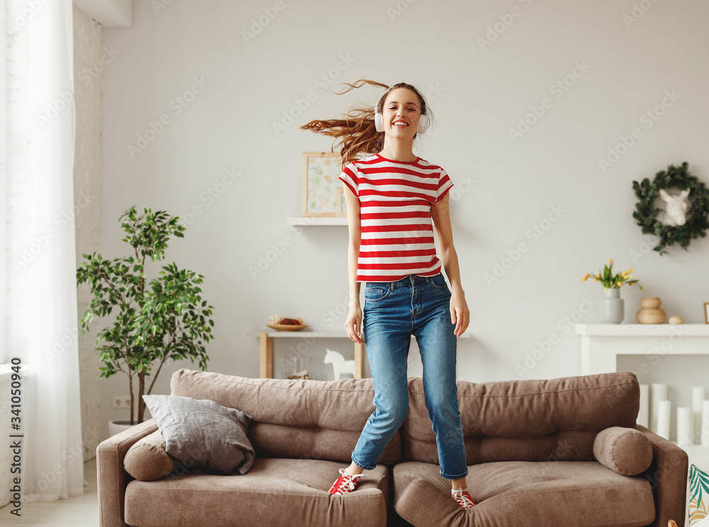 Happy woman listening to music and dancing on couch at home.