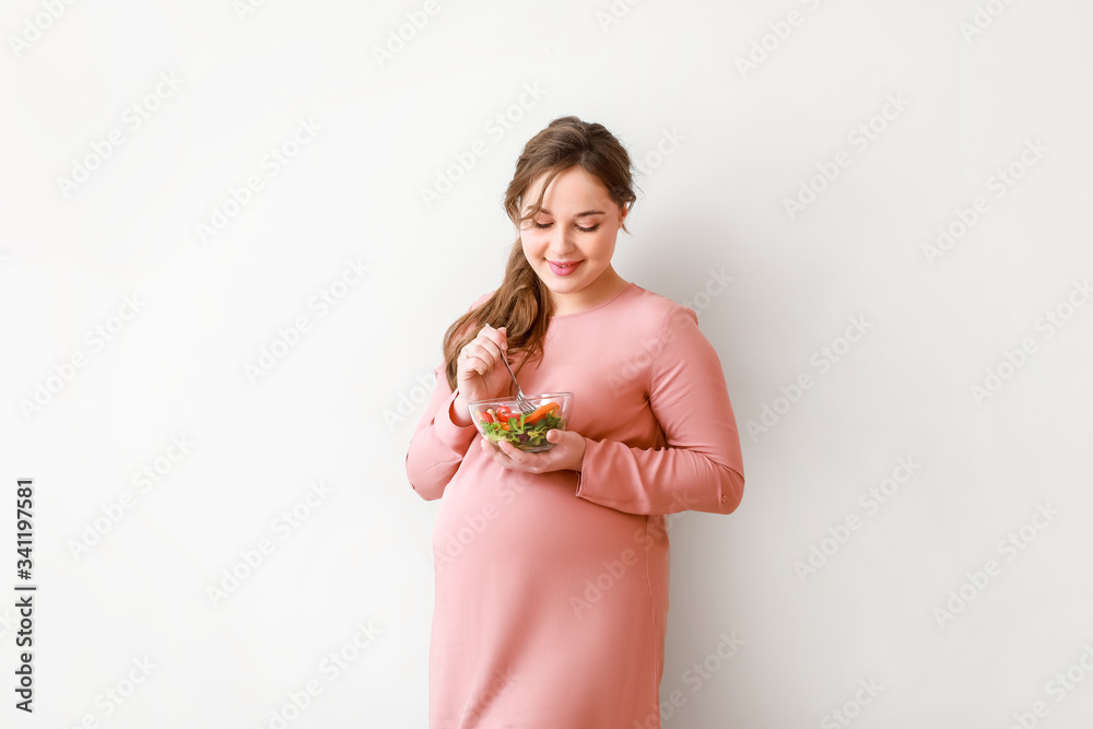 Beautiful pregnant woman with healthy salad on light background