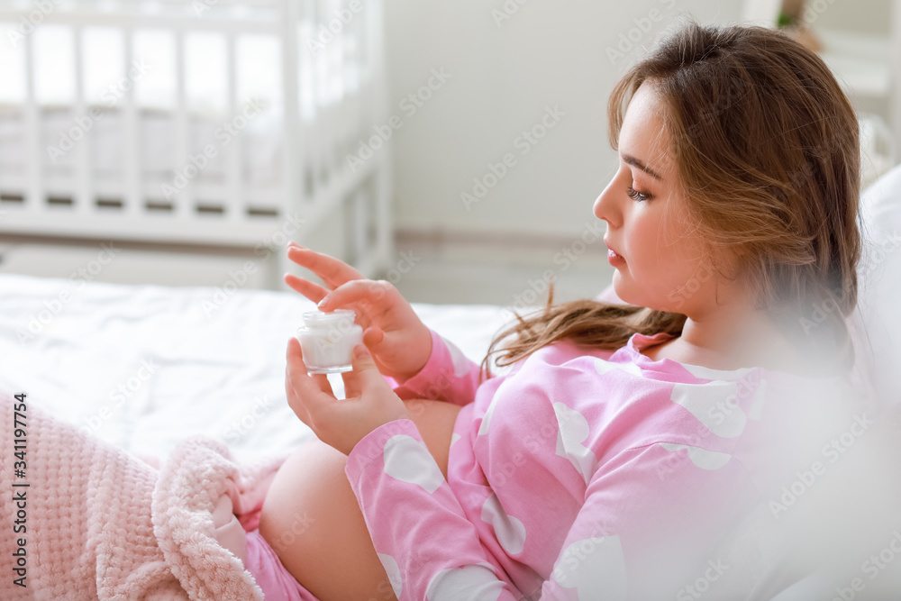 Beautiful pregnant woman applying cream at home