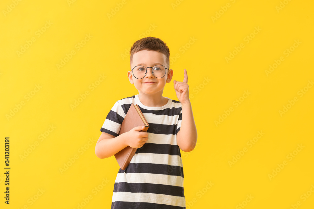 Cute little boy with book and raised index finger on color background