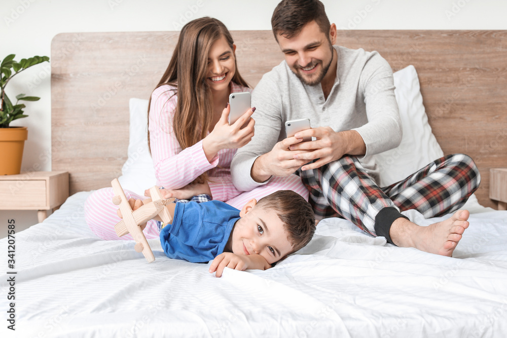 Little boy and his parents with mobile phones in bedroom