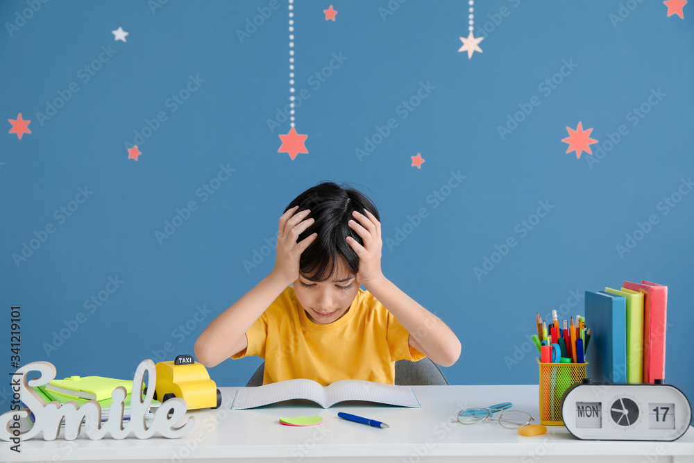 Stressed little boy doing homework against color background