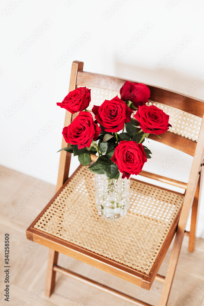 Red roses in a glass vase on a wooden chair