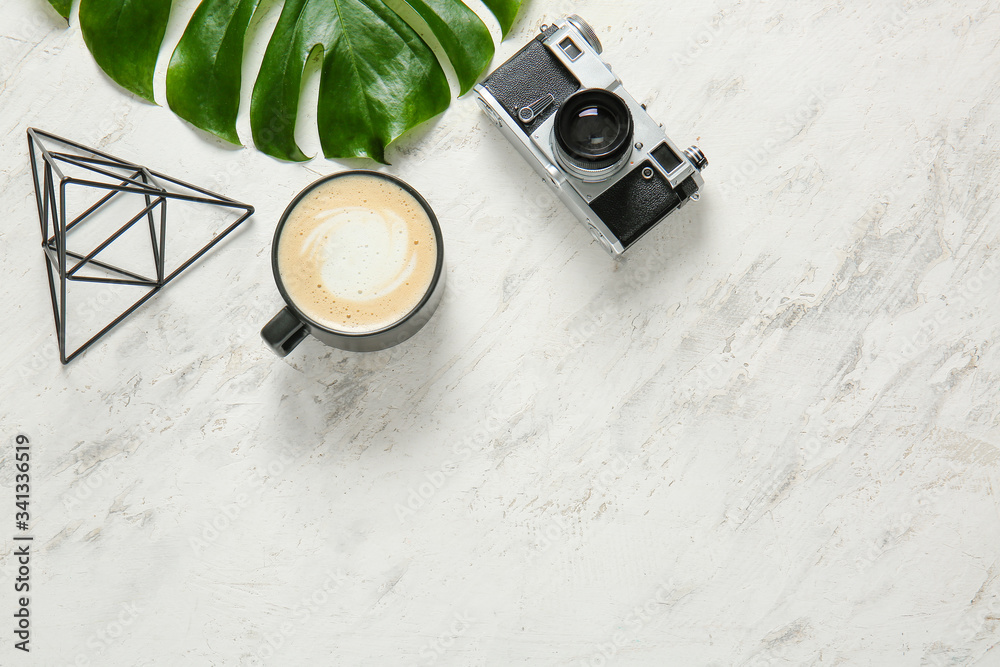 Cup of coffee, photo camera and tropical leaf on light background