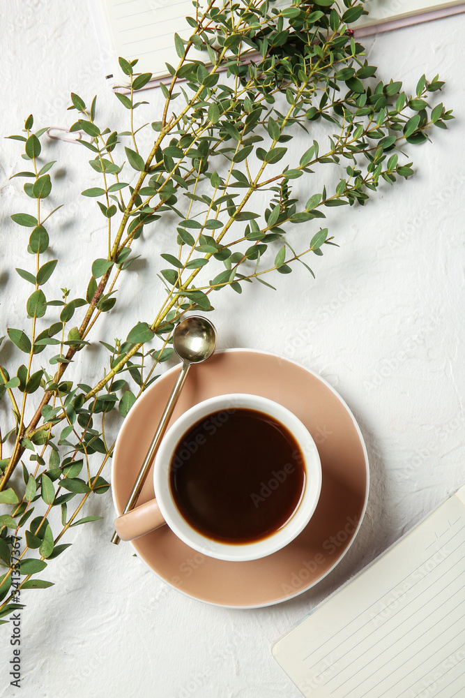 Cup of coffee and green branches on light background